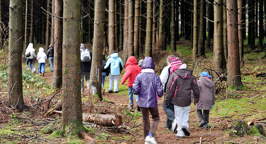 A lot of kids wearing winter cloths walking through the forest